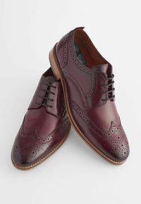 Chaussures en cuir bordeaux avec des détails brogue, un bout pointu et un laçage à cinq œillets. Semelle brune avec des accents cousus.