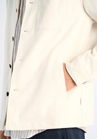 Krämfärgad jacka med framknäppning, bröstficka och sidofickor. Tillverkad av ett smidigt tyg med en ren design och minimal sömnad.