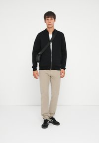 Sort zip-up bomberjakke med ribbede manchetter, beige slim fit bukser og sorte sneakers. Outfittet er fuldendt med en crossbody taske.