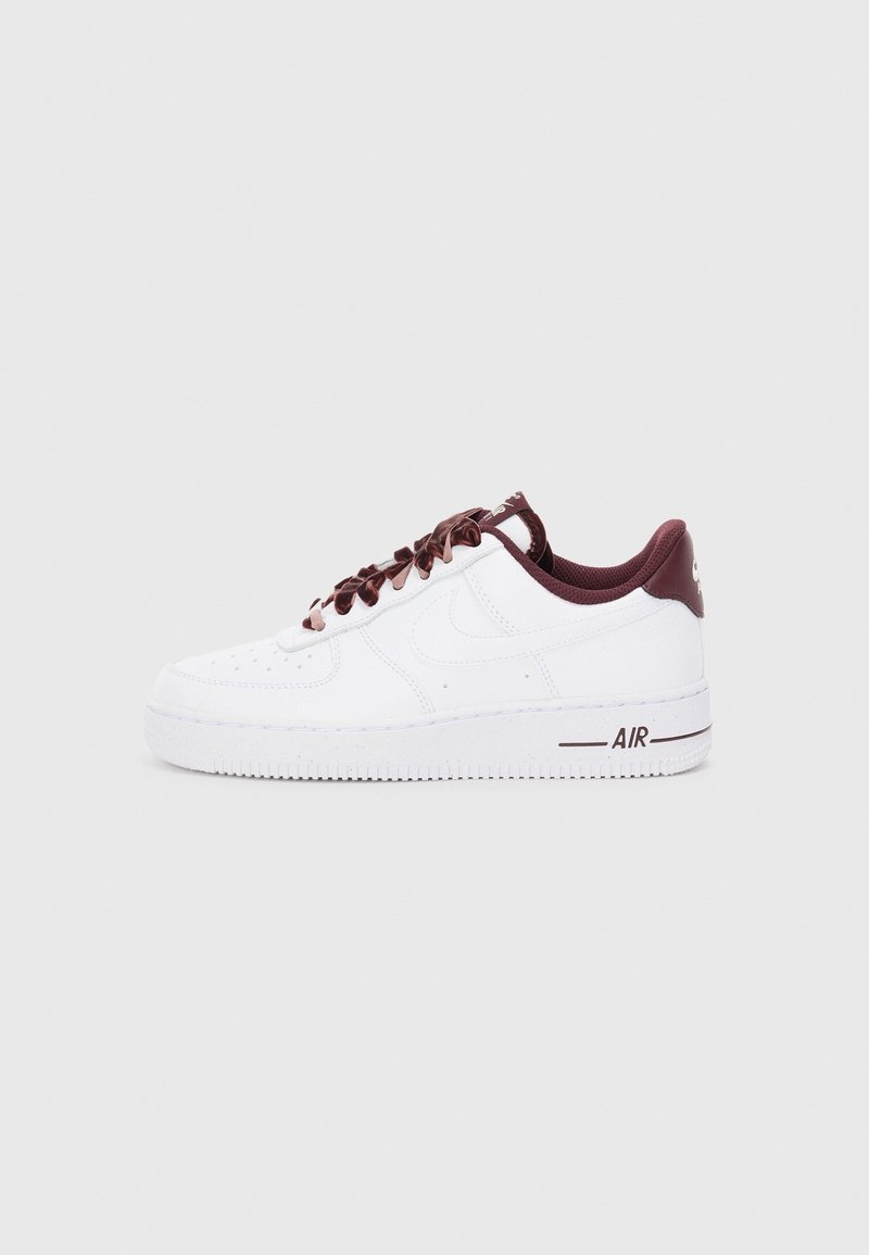 Baskets basses blanches avec des lacets, une doublure intérieure et un languette talonnière couleur bordeaux, avec une semelle marquée affichant le texte "AIR" sur le côté.