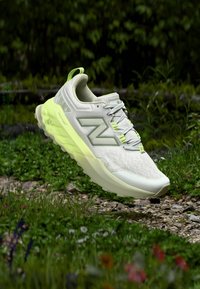 Hellgrauer Sneaker mit strukturierter Oberfläche, neon-gelben Akzenten und einer klobigen Sohle. Verfügt über ein auffälliges „N“-Logo und ein unterstützendes Design.