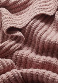 Tekstūras rozā adīts audums ar ribotu dizainu, kurā ieausti smalki metāliski diegi, piešķirot papildus detaļas un vizuālu interesi.