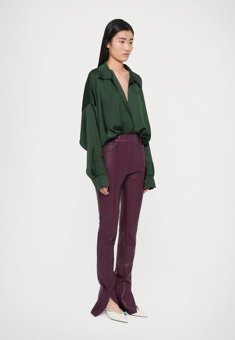 Green satin oversized shirt with a deep V-neck, paired with burgundy fitted leather pants featuring slits and white pointed-toe heels.