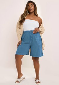 Blå bomullsshorts med avslappnad passform, iögonfallande sidfickor, knappstängning och en slät struktur, bära med en vit topp och en beige skjorta.