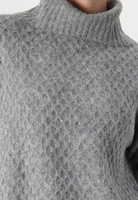 Šedý pletený svetr s vysokým žebrovaným límcem a texturovaným vzorem medové plástve. Měkký materiál s útulným vzhledem.