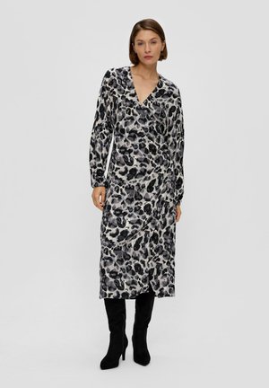 Langärmliges Kleid mit Leopardenmuster in Schwarz-, Grau- und Weißtönen, mit V-Ausschnitt und fließender Silhouette, kombiniert mit schwarzen hohen Stiefeln.