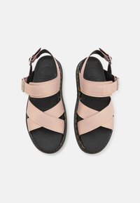 Różowe skórzane sandały z krzyżującymi się paskami i zapięciem na klamrę, z czarną podeszwą i żółtym przeszyciem. Gładka tekstura.