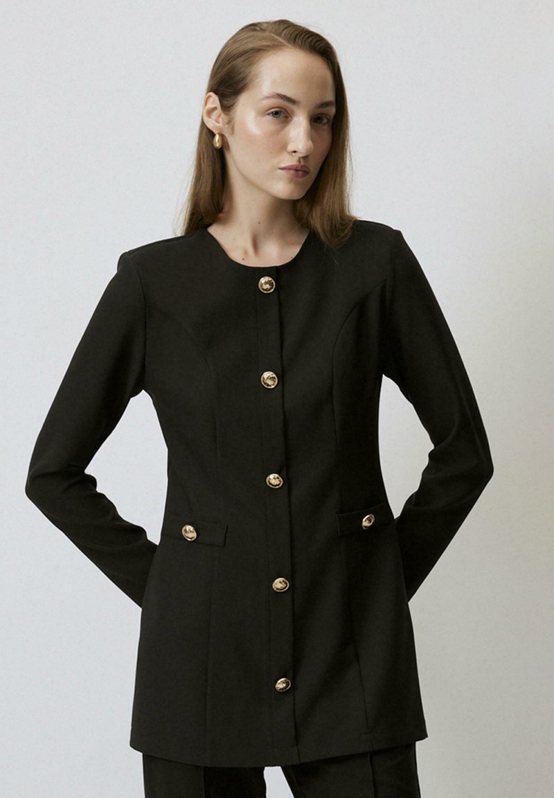 Black tailored blazer with a round neckline, six gold buttons down the front, and two side pockets. Smooth texture, structured fit.