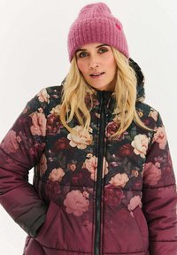 Květovaná péřová bunda s vínovým základem, zdobená velkými růžovými a krémovými květy. Doplněná růžovou pletenou čepicí.