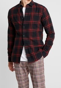 Langärmliges schwarz-rotes kariertes Hemd mit Knopfleiste, aus weichem Baumwollmaterial und mit lockerer Passform, kombiniert mit karierter Hose.
