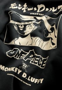 Czarna koszulka z materiału z białą grafiką przedstawiającą postać w słomkowym kapeluszu, z napisem "One Piece" i "Monkey D. Luffy" poniżej.