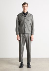 Grau karierte Jacke mit zwei Brusttaschen, Knopfleiste und langen Ärmeln, kombiniert mit passenden grau karierten Hosen und schwarzen Schuhen.