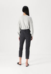 Suéter cinza texturizado sobre jeans cinza escuro de cintura alta com punhos enrolados e bolsos traseiros, combinado com sapatilhas pretas sem salto.