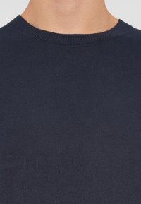 Sweater de malha azul marinho com decote redondo e detalhes em canalé. Textura suave, costura uniforme e sem padrões ou acentos visíveis.
