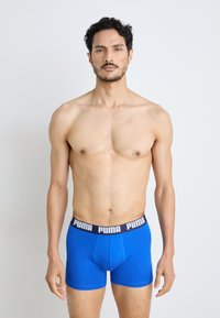 Kék pamut boxer alsó, fekete elasztikus derékpánttal, rajta fehér "PUMA" logóval. A szabás szoros és az anyag simának tűnik.
