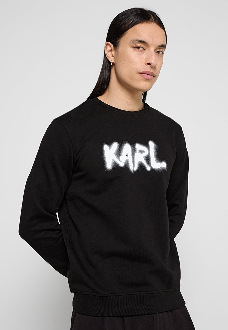 Sudadera negra de mezcla de algodón, con un logo "KARL" en spray blanco en la parte frontal. Cuello y puños acanalados, corte relajado.