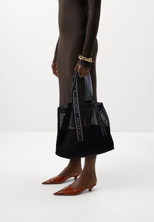 Svart netting totebag med doble stoffstropper som har hvit merkevare. Vesken er strukturert og romslig, supplert med enkle metalliske detaljer.