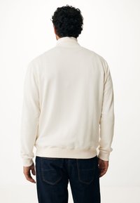 Sudadera color crema con cuello alto, puños y dobladillo canalé. Combinada con jeans azul oscuro, mostrando una textura suave y lisas.