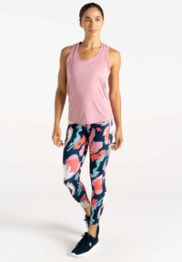 Hellrosa ärmelloses Oberteil, kombiniert mit enganliegenden Leggings mit einem abstrakten Muster in Navy, Pink und Weiß, und schwarzen Sportschuhen.