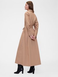 Rochie lungă bej dintr-un material ușor, cu guler, talie strânsă și croi lejer, combinată cu cizme negre cu toc înalt.