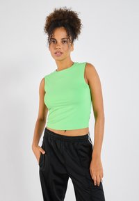 Short-sleeve, bright green crop top made of smooth fabric. Paired with black athletic pants featuring white side stripes.