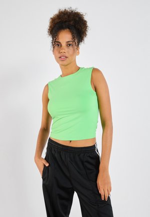 Top scurt cu maneci, de culoare verde deschis, realizat dintr-un material neted. Asortat cu pantaloni sport negri cu dungi albe pe laterale.