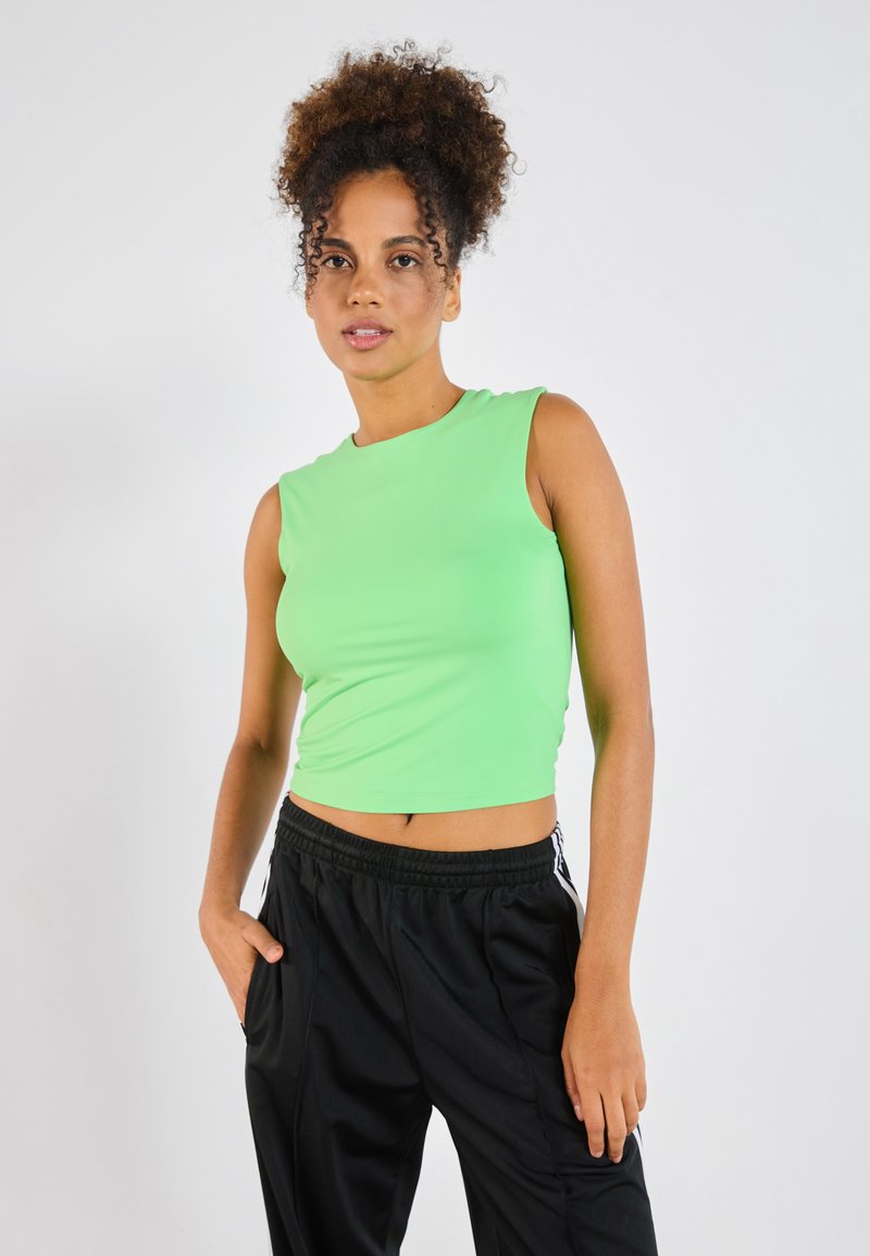 Short-sleeve, bright green crop top made of smooth fabric. Paired with black athletic pants featuring white side stripes.