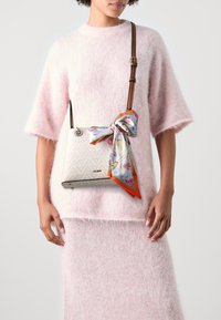 Vit läderhinkväska med rosa blommig silkesduk knuten vid handtaget. Texturerat fiskbensmönster och brun justerbar rem.