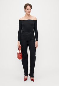 Fekete, vállra csúsztatható felső, magas derekú sötét farmernadrág, piros kézitáska és piros hegyes orrú magassarkú cipő. Finom fényességgel és strukturált szabással rendelkezik.