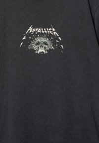 Černé tričko vyrobené z bavlny s grafickým designem lebky a stylizovaným nápisem "Metallica" nad ní.