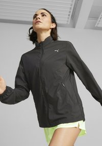 Sort letvægtsjakke med høj krave, lynlåslommer og elastiske manchetter. Har et lille hvidt logo på brystet.