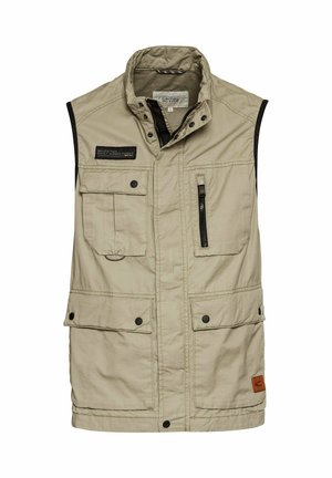 Beige ärmellose Weste aus strapazierfähigem Material, ausgestattet mit mehreren Taschen, einer mitReißverschluss und einem Markenlabel auf der Brust.