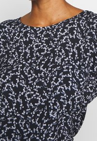 Tessuto nero con un motivo floreale bianco caratterizzato da piccoli fiori e rami sottili, texture liscia, scollatura leggermente arrotondata.