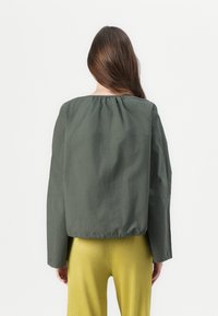 Veste verte légère avec un col froncé et une coupe ample. Équipée de manches longues et d'un ourlet élastiqué. Assortie à un pantalon jaune à côtes.