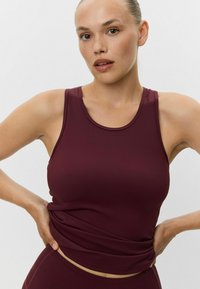 Burgundský športový top s okrúhlym výstrihom, vyrobený z elastického materiálu, ktorý má priliehajúci strih a hladkú textúru.