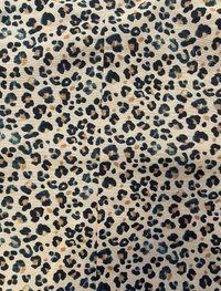 Leopardenmusterstoff hat einen beigefarbenen Hintergrund mit schwarzen und grauen Flecken, akzentuiert von braunen Schattierungen, und verfügt über eine weiche, strukturierte Oberfläche.