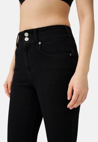Jeans neri a vita alta con vestibilità slim, due bottoni metallici e tasche classiche con dettagli di cucitura discreti.