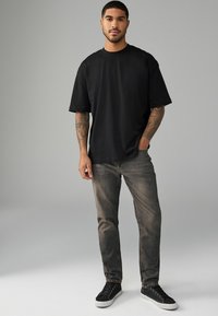 Tricou oversized negru din bumbac, asortat cu blugi gri estompati și adidași negri cu talpă din cauciuc albă și design cu șireturi.