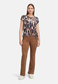 Rövid ujjú, testhez simuló állatmintás top sötét színekben, csomózott szegéllyel; barnás süet-szerű bővülő nadrággal és fehér tornacipővel párosítva.