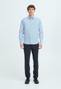 Cămașă butonată de un albastru deschis, cu un model subtil, asortată cu pantaloni închiși la culoare și pantofi negri. Material din bumbac, mâneci lungi, croială clasică.