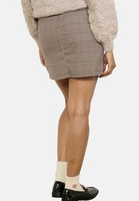 Tailored mini skirt with a brown and cream houndstooth pattern, featuring a straight cut and waistband. Paired with white socks and black loafers.
