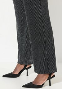 Zwarte hoge hakken slingback schoenen met een spitse neus en textuurdetails, gecombineerd met zwarte broek met verticale zilveren strepen.