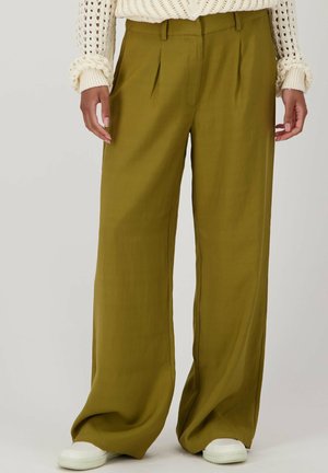 Olijfgroene wijdvallende broek met plooien aan de voorkant, gemaakt van lichte stof, gecombineerd met witte gestructureerde sneakers.