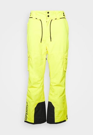 Pantalon de neige jaune vif avec poignets renforcés noirs, poches avant, passants de ceinture et logo Superdry près du bas de la jambe gauche.
