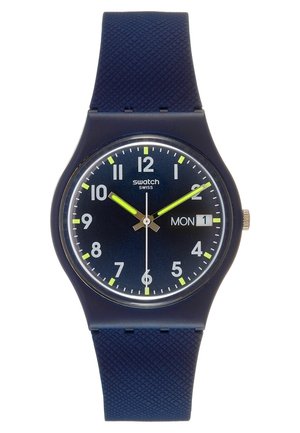 Dunkelblaue Swatch-Armbanduhr mit neongelben Zeigern, weißen Stundenmarkierungen und einer Tagesdatumsanzeige, die Montag, den 1. zeigt.