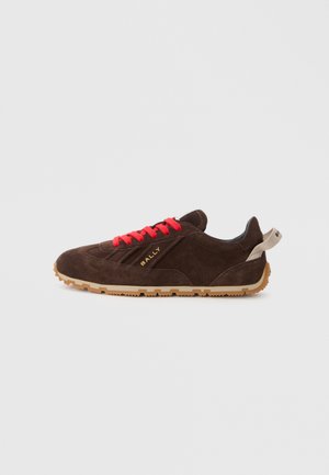 Braune Wildledersneaker mit roten Schnürsenkeln, Gummisohle und goldener Logoprint. Merkmale sind eine runde Zehenpartie und eine weiche, strukturierte Oberfläche.