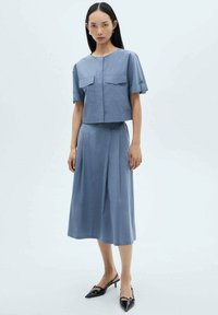 Blue cropped top with two chest pockets paired with a matching midi skirt. The fabric has a smooth texture. Worn with black heeled shoes.