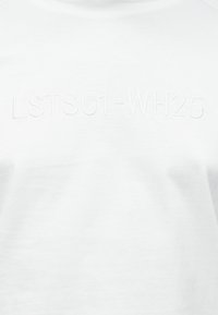 Baltas medvilninis marškinėlis su reljefiniu užrašu "LSTS01-WH25" priekyje, apvalia iškirpte ir trumpomis rankovėmis. Lygios tekstūros.