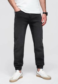 Jeans jogger negros de denim, con puños elásticos, bolsillos frontales y un diseño ajustado, combinados con zapatillas blancas.