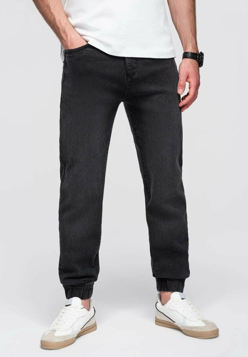 Musta juoksuhousut denimestä, joissa on elastiset hihnat, etutaskut ja slim fit -muotoilu, yhdistettynä valkoisiin lenkkareihin.